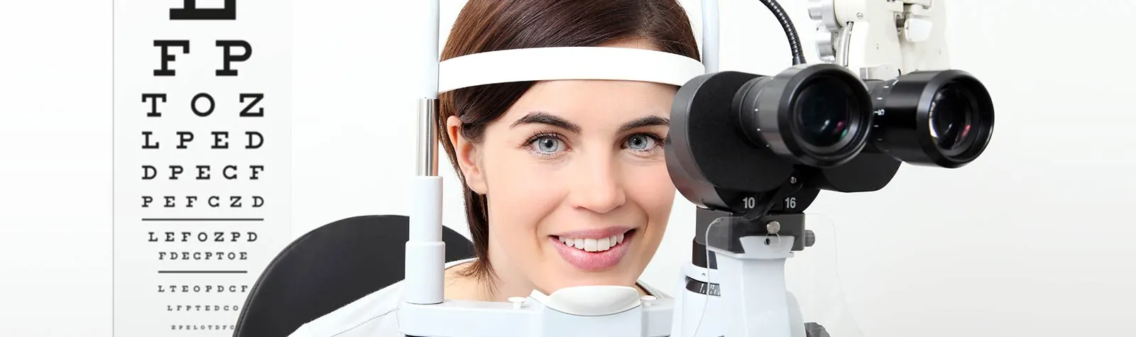 A woman at the phoropter in front of an eye chart — banner photo from the current why choose us page