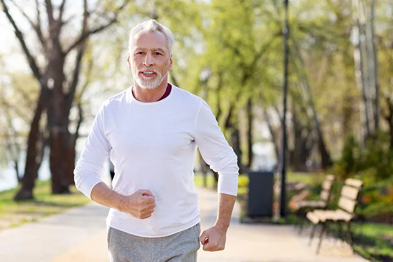 A man in his sixties walking through a park on a clear day